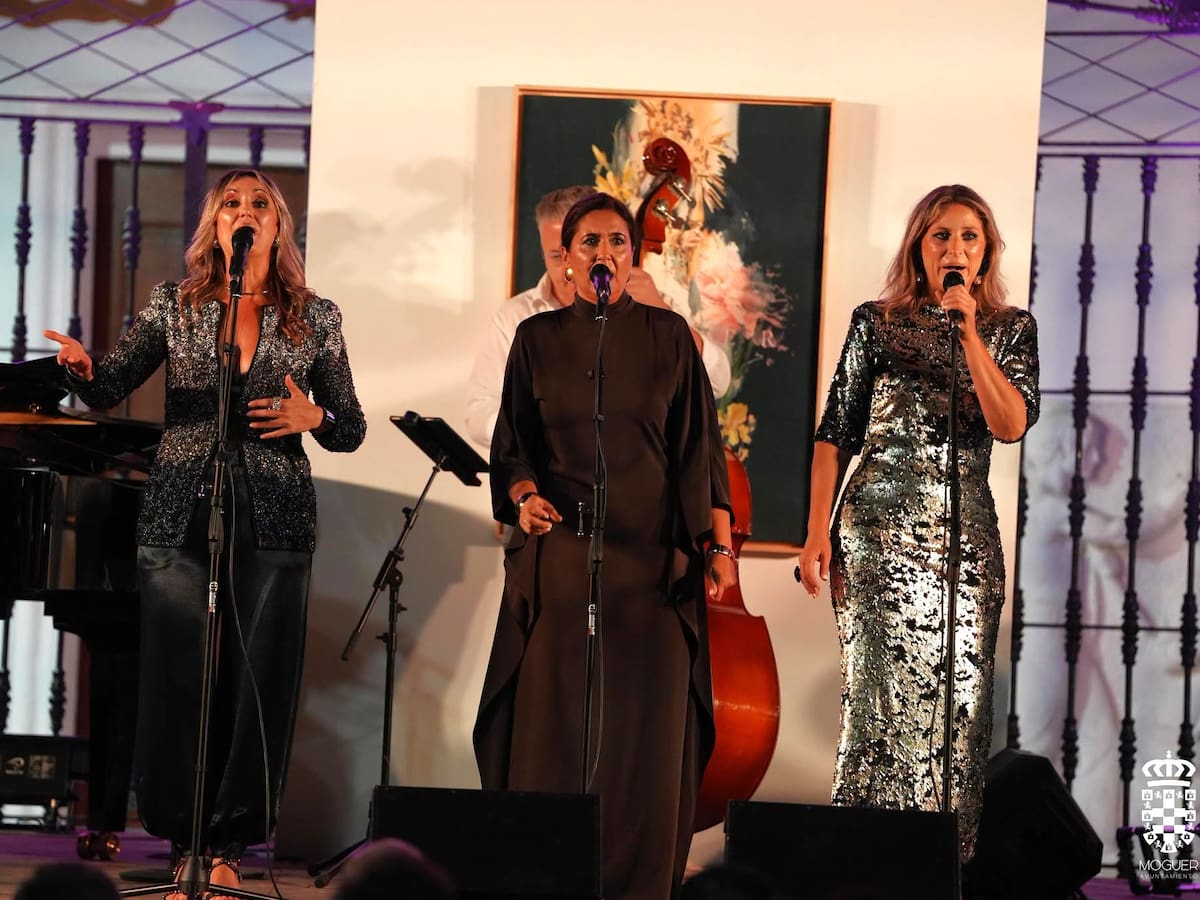 Tres cantantes interpretan el concierto del Pórtico de la Velada de Moguer frente al cartel de las fiestas.